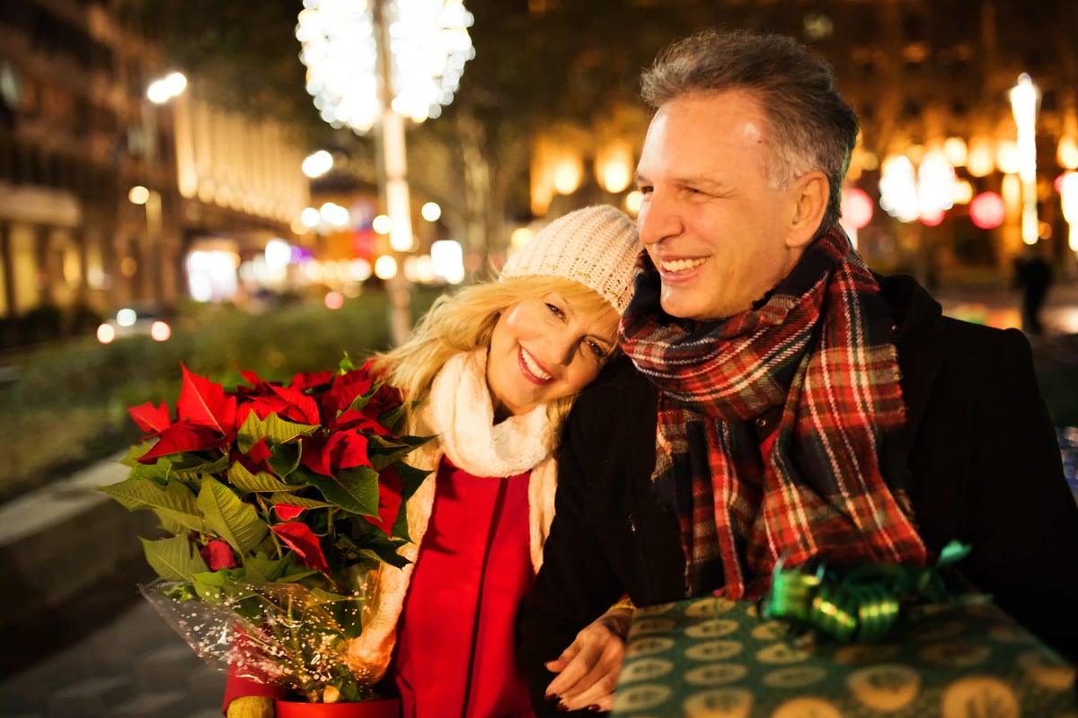 Paar mit Geschenk und Blumen in festlich beleuchteter Strasse bei Nacht