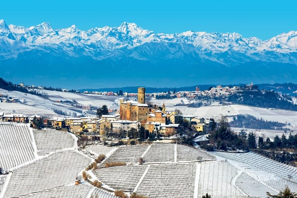 Winterliche Landschaft im Piemont mit Dorf, Weinbergen und schneebedeckten Alpen