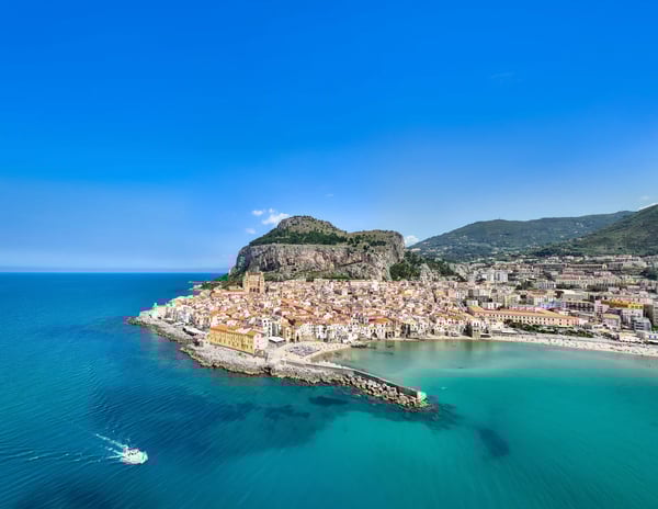 Luftaufnahme der Bucht von Cefalu mit Altstadt, Strand, Hafenmauer und tiefblauem Mittelmeer