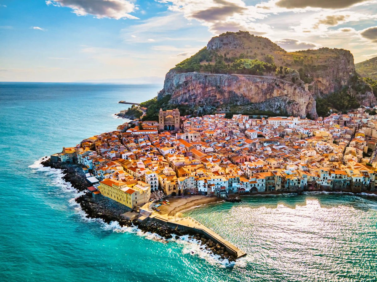 Historische Altstadt von Cefalu mit dicht bebauten Häusern am Meer und markantem Felsen im Hintergrund