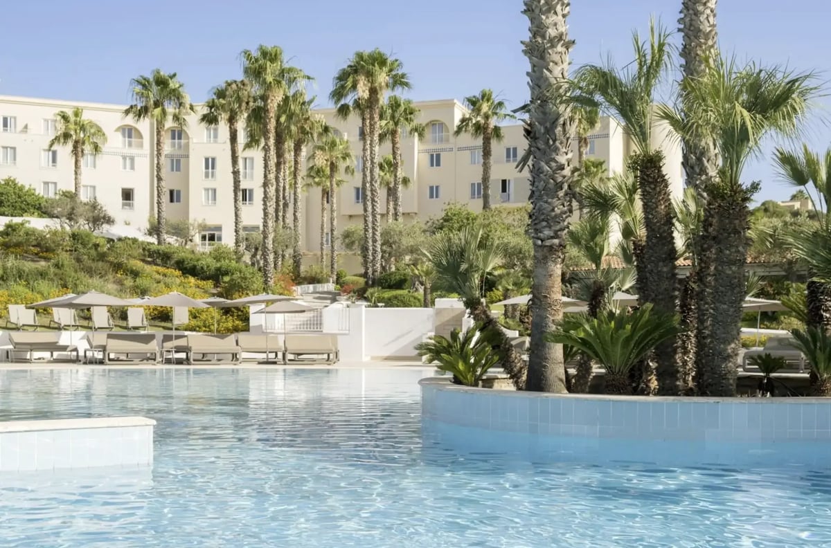 Hotelanlage mit grossem Pool, Palmen, Liegen und hellem Gebäude im Hintergrund