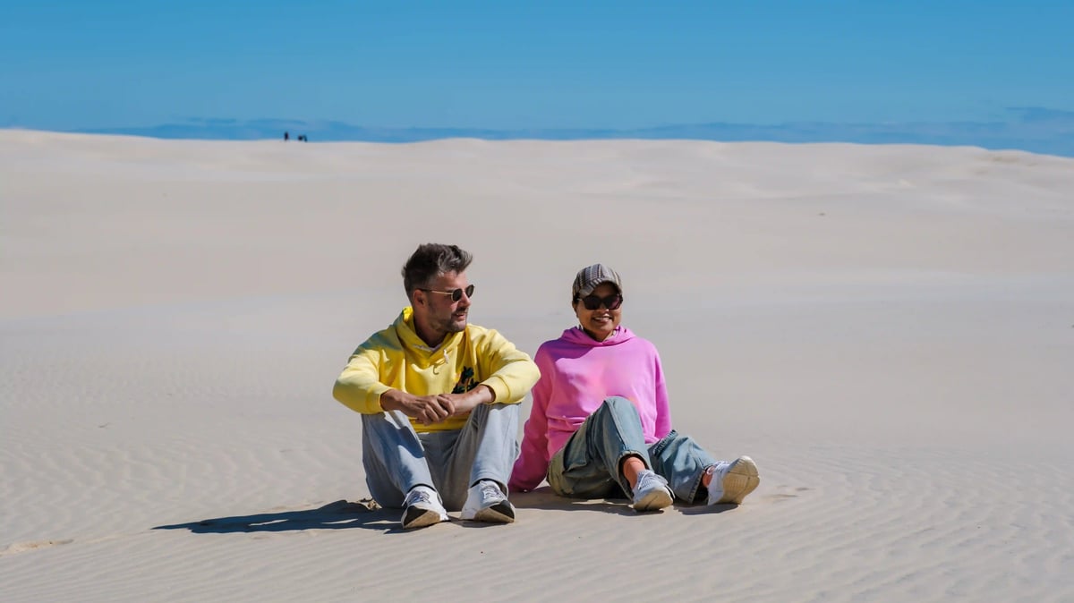 Paar sitzt entspannt in hellen Sanddünen am Meer bei sonnigem Wetter
