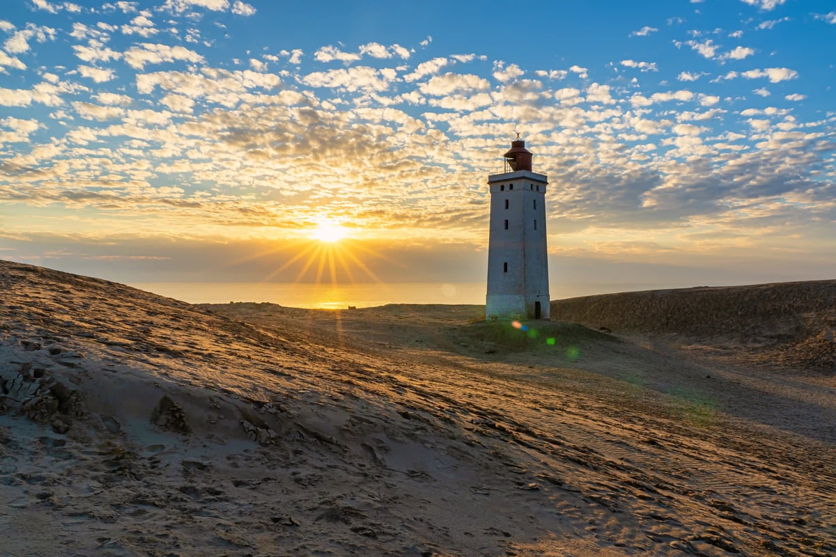 Leuchtturm auf sandiger Dünenlandschaft bei Sonnenuntergang mit Blick auf das Meer