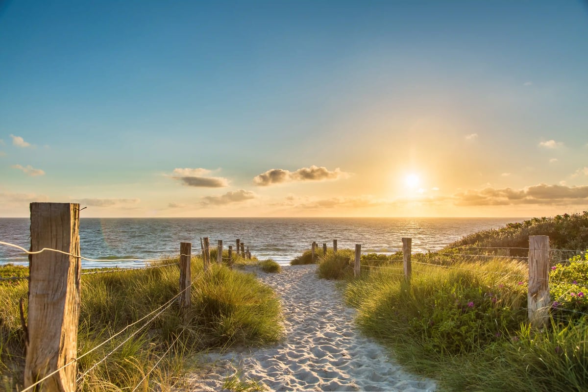 Sandweg durch begrünte Dünen führt zum Meer bei tief stehender Sonne