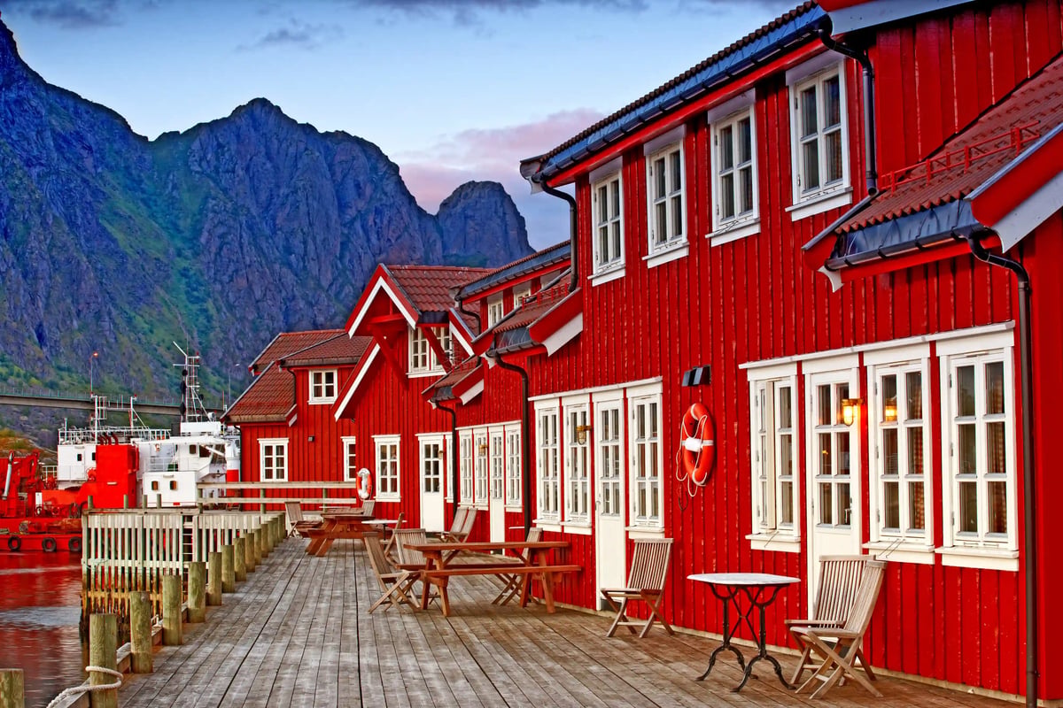 Rote Holzhäuser der Anker Brygge in Svolvaer stehen auf einem Holzsteg am Wasser vor steiler Bergkulisse