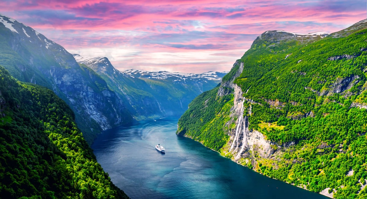 Panoramablick auf den Geirangerfjord mit steilen grünen Berghängen, Wasserfall und Kreuzfahrtschiff im Fjord