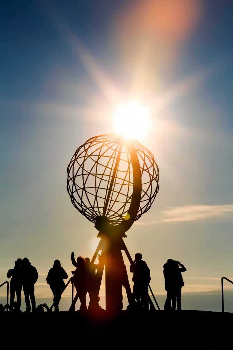 Nordkap Globusdenkmal vor tief stehender Sonne mit silhouettierten Menschen auf der Plattform