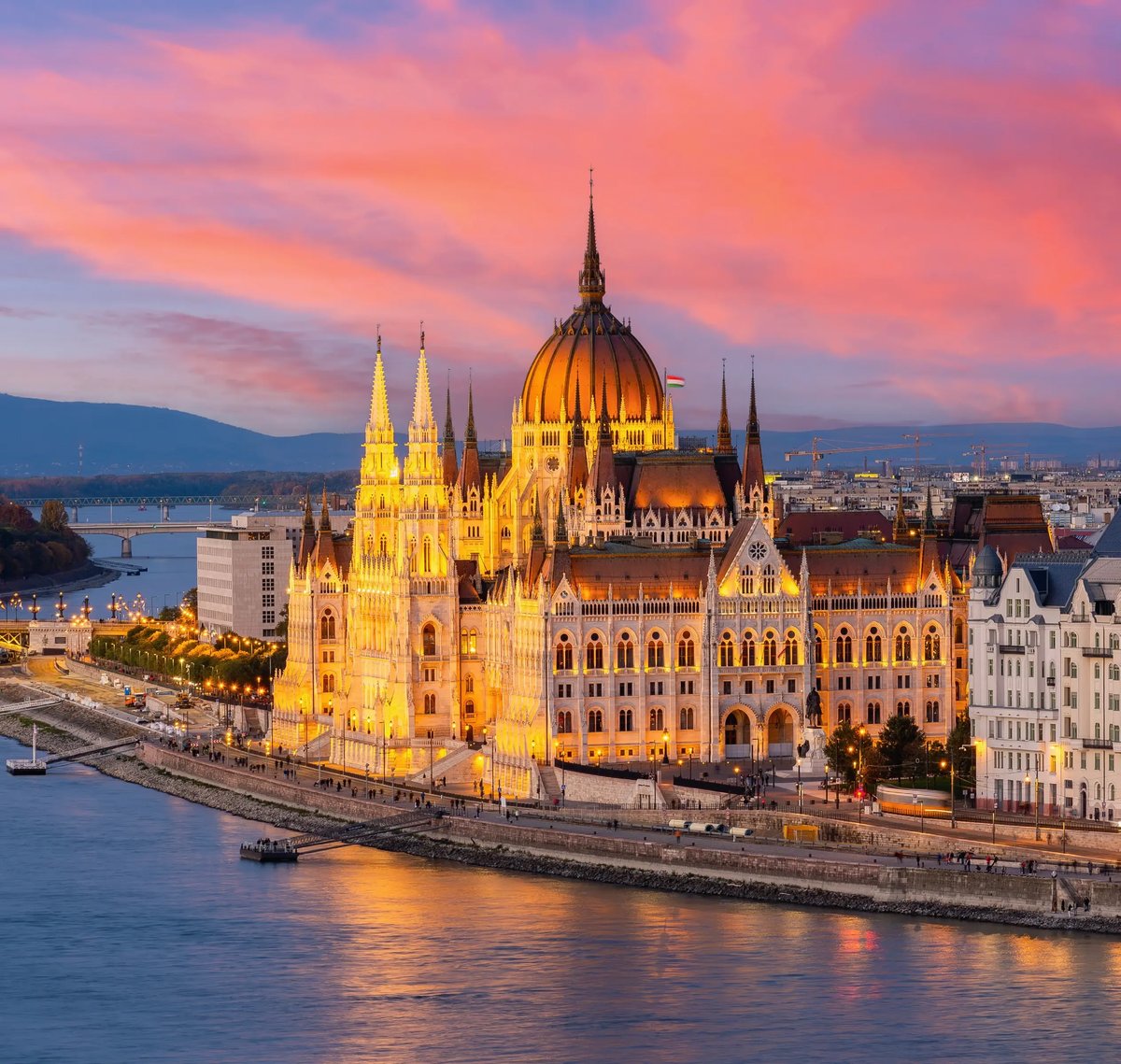 Das beleuchtete ungarische Parlamentsgebäude am Donauufer in Budapest bei Sonnenuntergang.