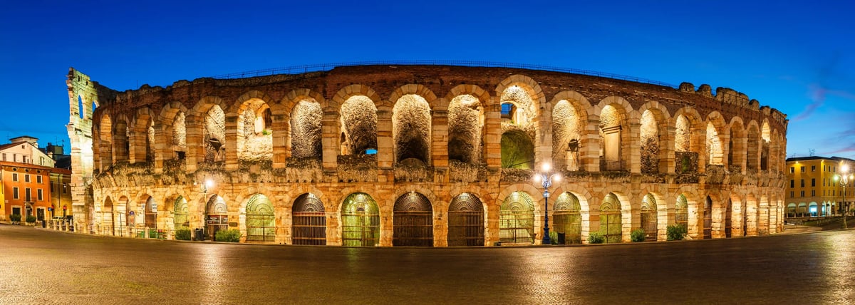 Beleuchtete Arena di Verona bei Nacht mit mächtigen Steinbögen und leerem Platz im Vordergrund