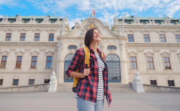 Junge Frau mit Rucksack steht vor historischem Gebäude und blickt lächelnd nach oben