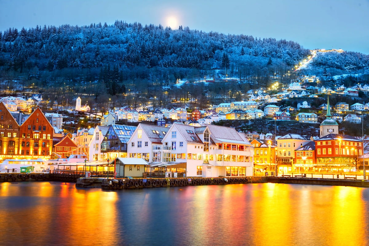 Winterliches Bergen mit beleuchtetem Hafen, bunten Häusern und schneebedeckten Hügeln. FR:
