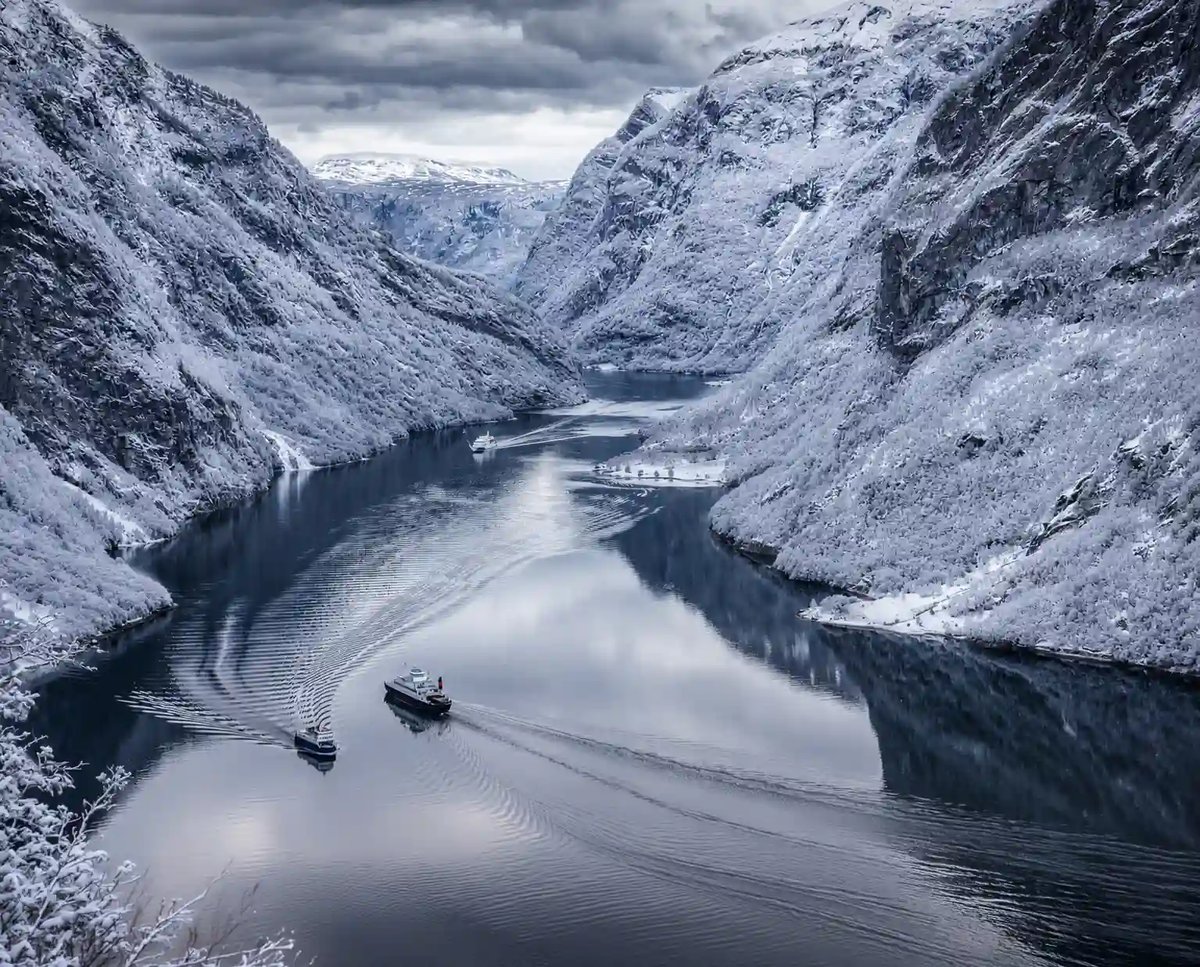 Verschneiter Nærøyfjord mit steilen Bergen und Schiffen auf dem ruhigen Wasser.