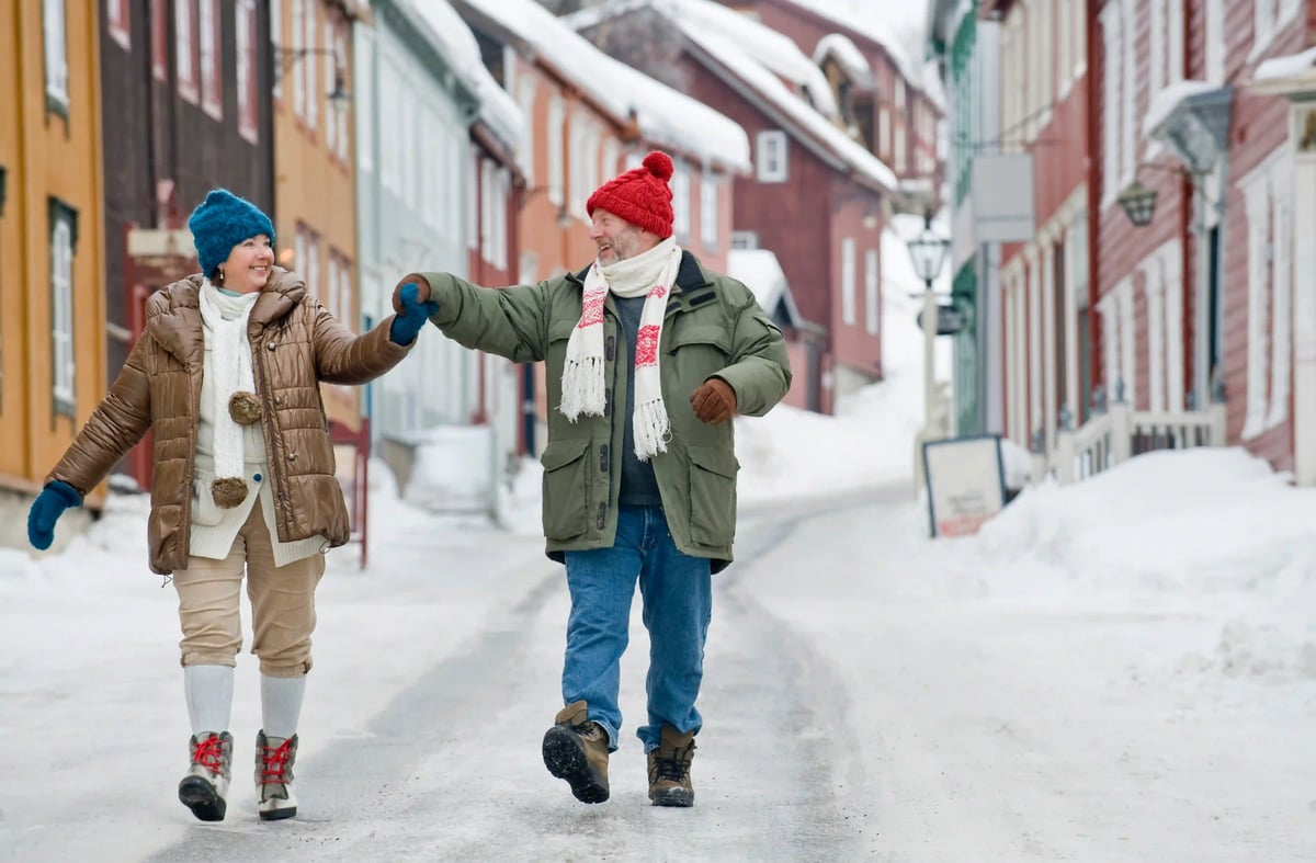 Glückliches Paar spaziert durch eine verschneite Strasse mit bunten Holzhäusern.