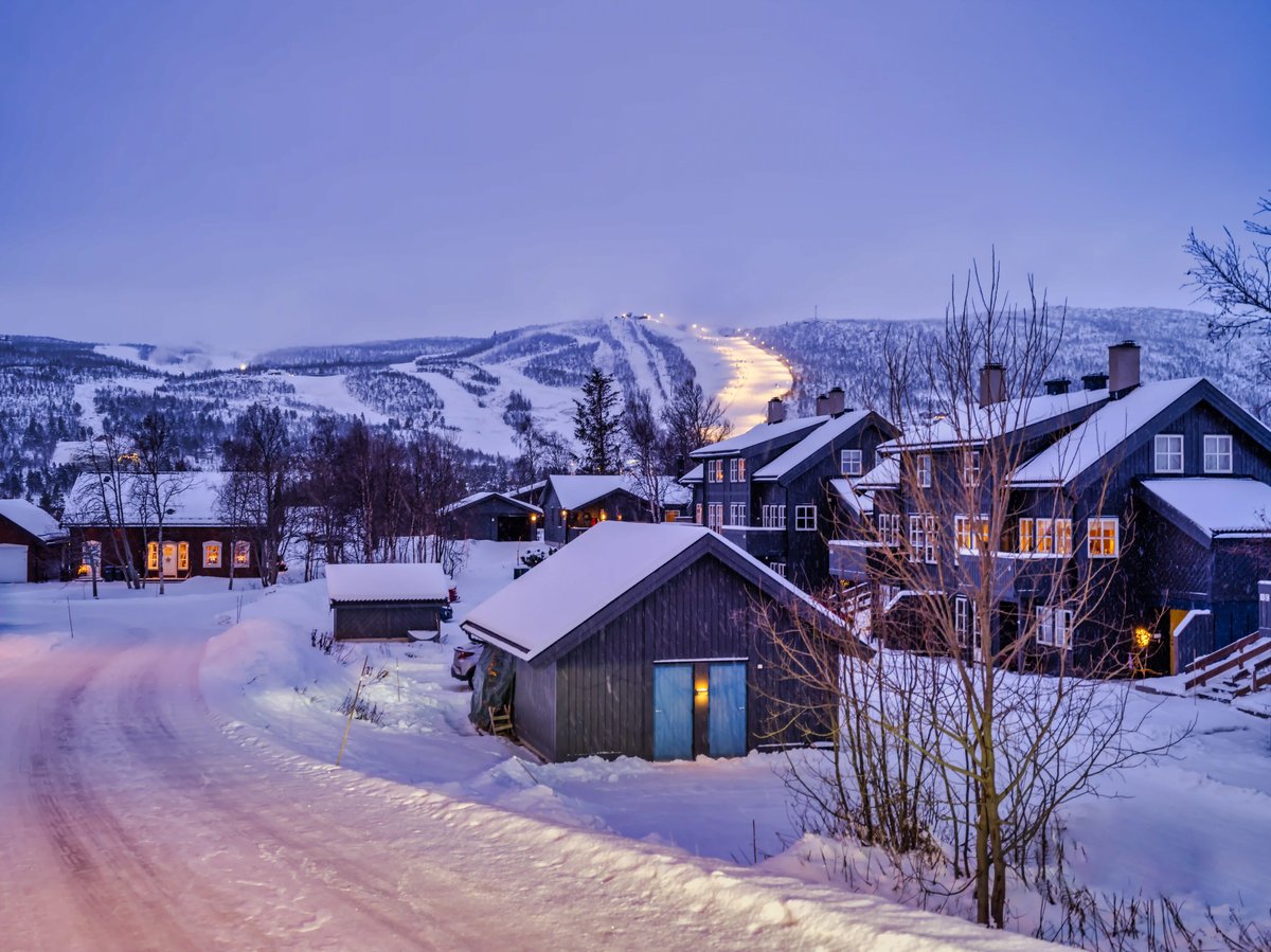 Verschneites Geilo mit Holzhäusern und beleuchteten Skipisten im Hintergrund.