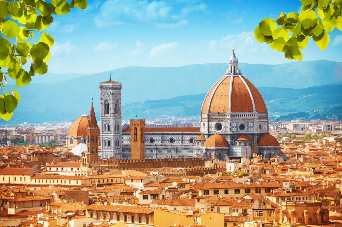 Panorama de Florence avec la cathédrale Santa Maria del Fiore et sa grande coupole rouge, avec des collines et des montagnes sous un ciel bleu.