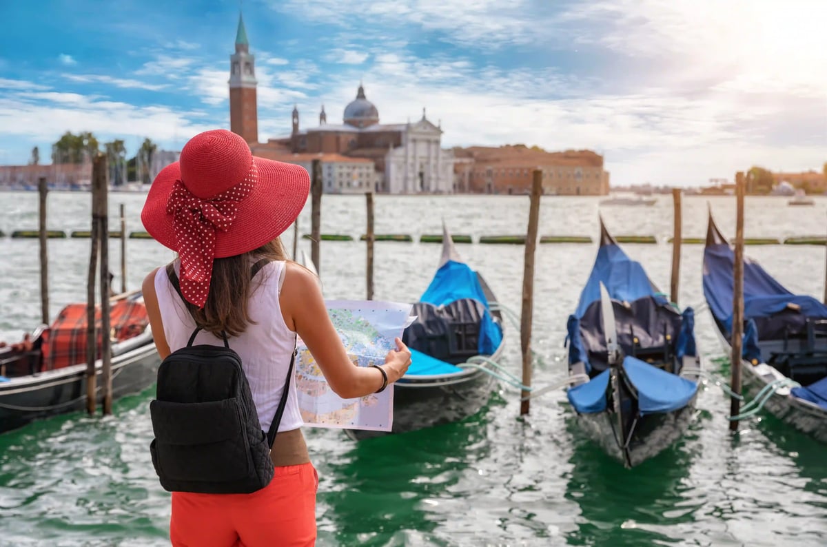 Frau mit rotem Hut hält einen Stadtplan und blickt auf Gondeln und die Kirche San Giorgio Maggiore in Venedig