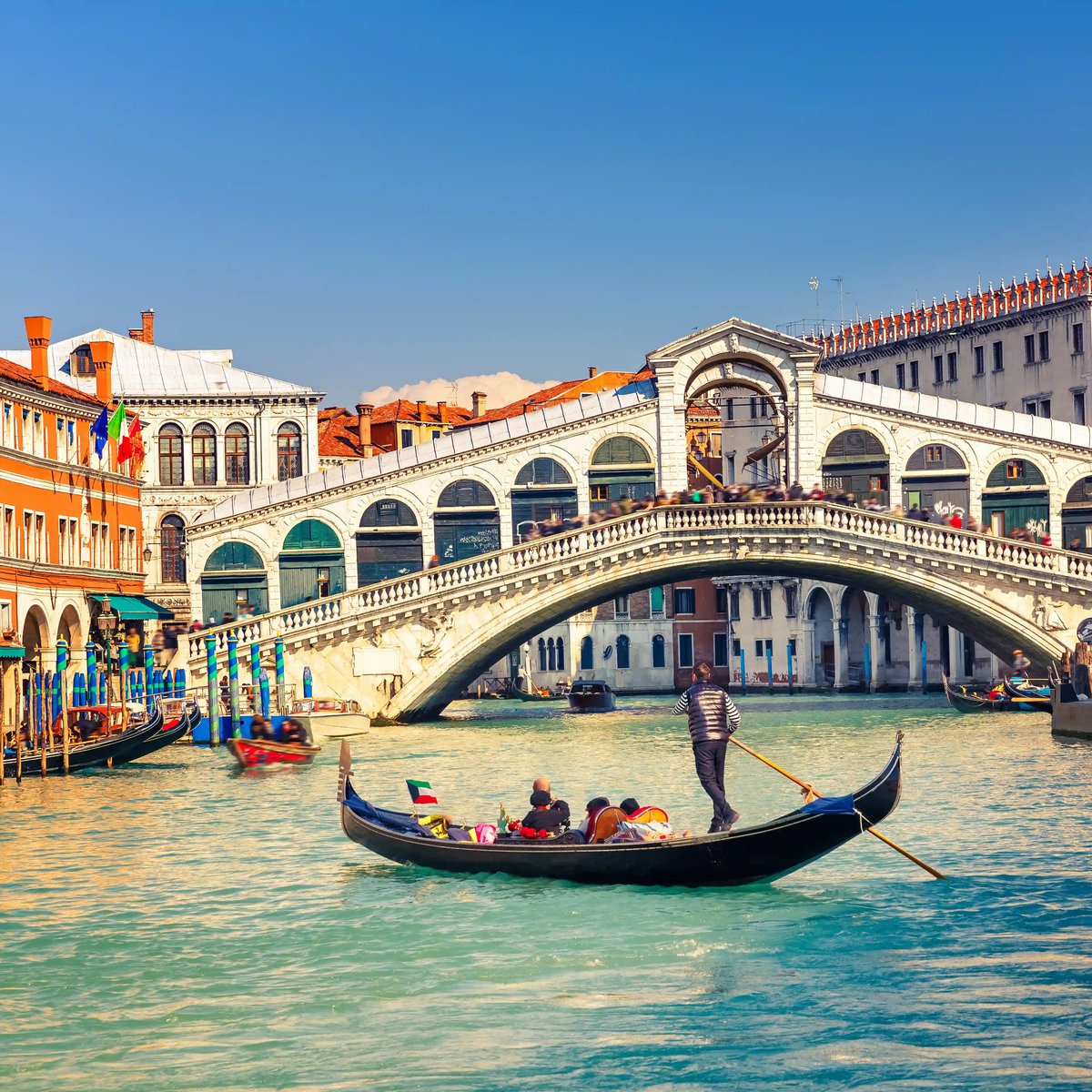 Rialtobrücke in Venedig mit Gondel im Vordergrund und Passanten auf der historischen Steinbrücke über dem Canal Grande