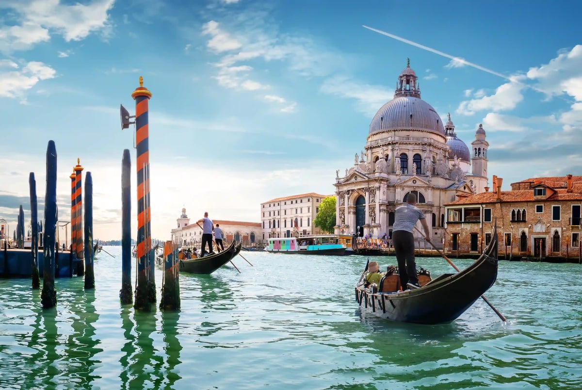 Gondeln gleiten über das Wasser der Lagune von Venedig vor der Kirche Santa Maria della Salute bei hellem Tageslicht