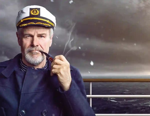 Älterer Kapitän in Uniform raucht Pfeife an Deck eines Schiffes bei stürmischer See