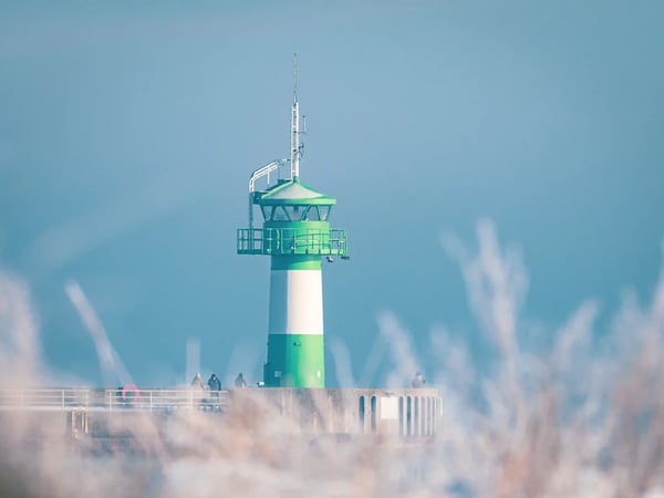 Grün weisser Leuchtturm von Travemünde an der Ostsee mit Spaziergängern im Vordergrund