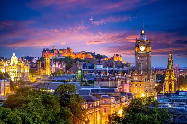 Beleuchtetes Stadtpanorama von Edinburgh mit historischen Gebäuden, Uhrturm und Burg bei farbigem Abendhimmel