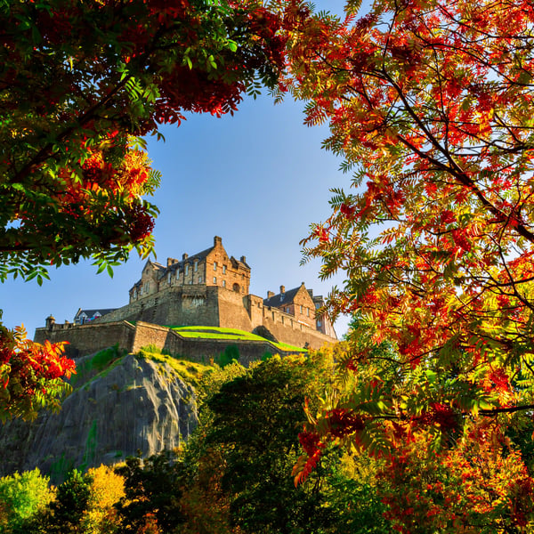 Edinburgh Castle auf einem Felsen, eingerahmt von herbstlich gefärbten Bäumen unter blauem Himmel
