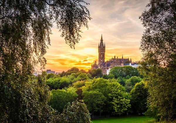 Universitätsgebäude von Glasgow ragt über grüne Parklandschaft bei goldenem Sonnenuntergang