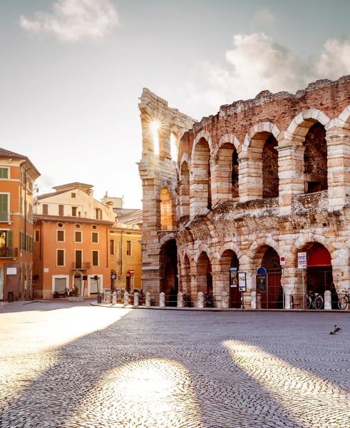 Römisches Amphitheater in Verona mit hohen Steinarkaden, angrenzenden Altstadthäusern und Sonnenlicht auf dem gepflasterten Platz.