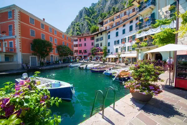 Kleiner Hafen in Limone mit bunten Häusern, Booten im smaragdgrünen Wasser und steilen Felsen im Hintergrund.
