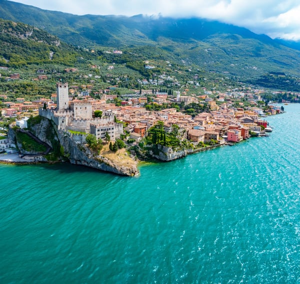 Blick auf die Scaligerburg von Malcesine mit Burganlage auf einem Felsen über dem Gardasee und umliegender Altstadt.