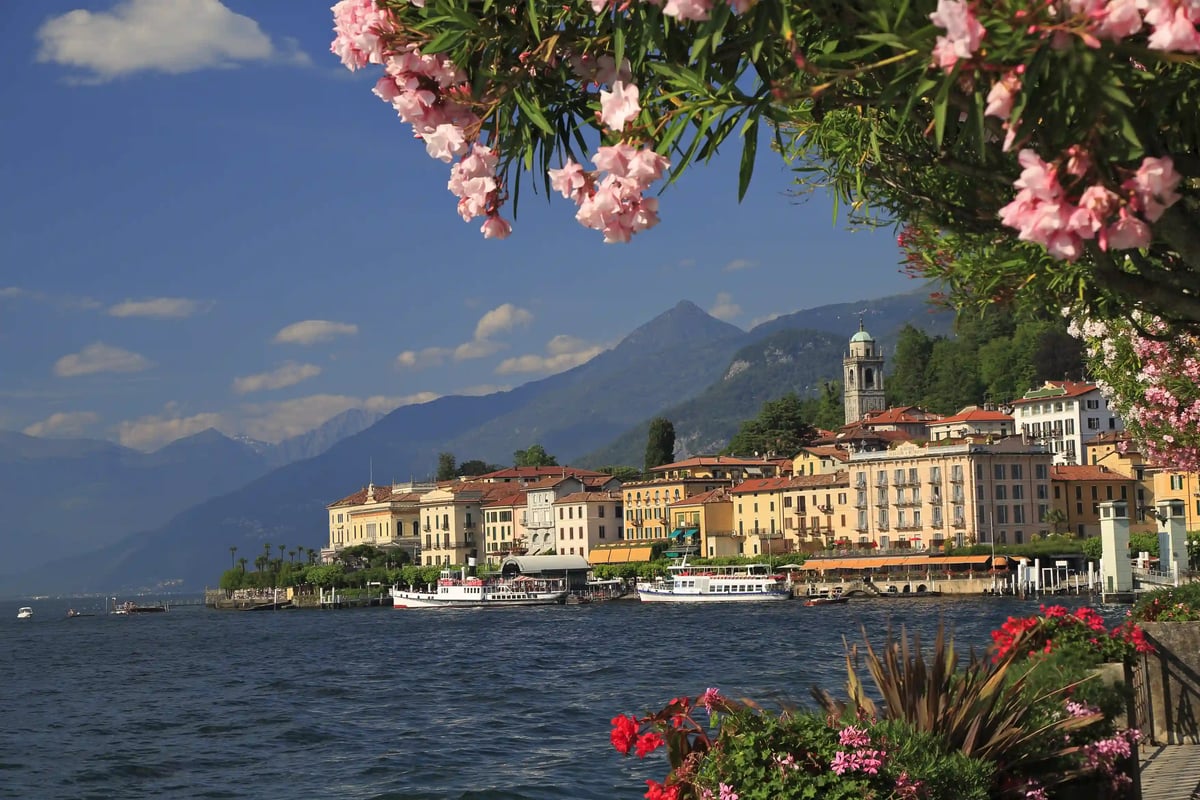 Farbenfrohe Häuser von Bellagio am Comersee vor Alpen und blühenden Pflanzen