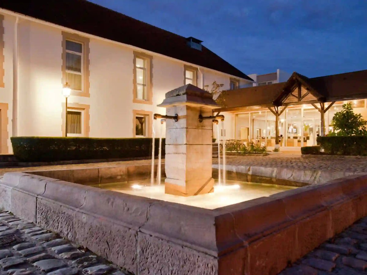 Beleuchteter Innenhof eines Hotels mit rechteckigem Brunnen und modernem Gebäude in den Abendstunden