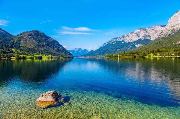 Klarer Grundlsee mit spiegelnden Alpen und grünem Ufer bei Sonnenschein