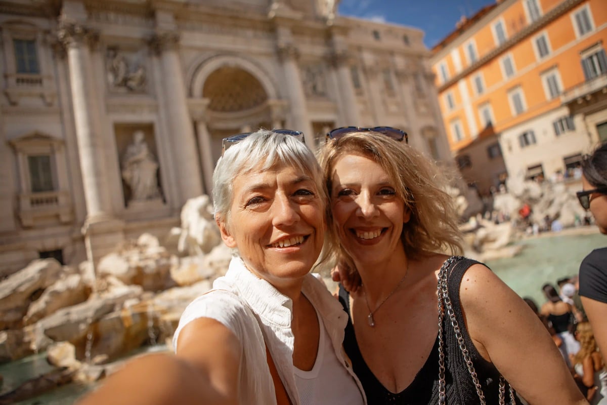 Deux femmes souriantes prennent un selfie devant la fontaine de Trevi à Rome par beau temps