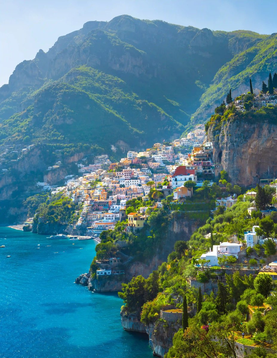 Maisons colorées de la côte amalfitaine accrochées à des falaises abruptes au dessus de la mer turquoise avec collines verdoyantes en arrière plan