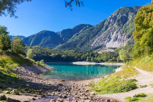 Türkiser Bergsee mit klarem Wasser, umgeben von bewaldeten Hängen und steilen Felswänden unter wolkenlosem Himmel
