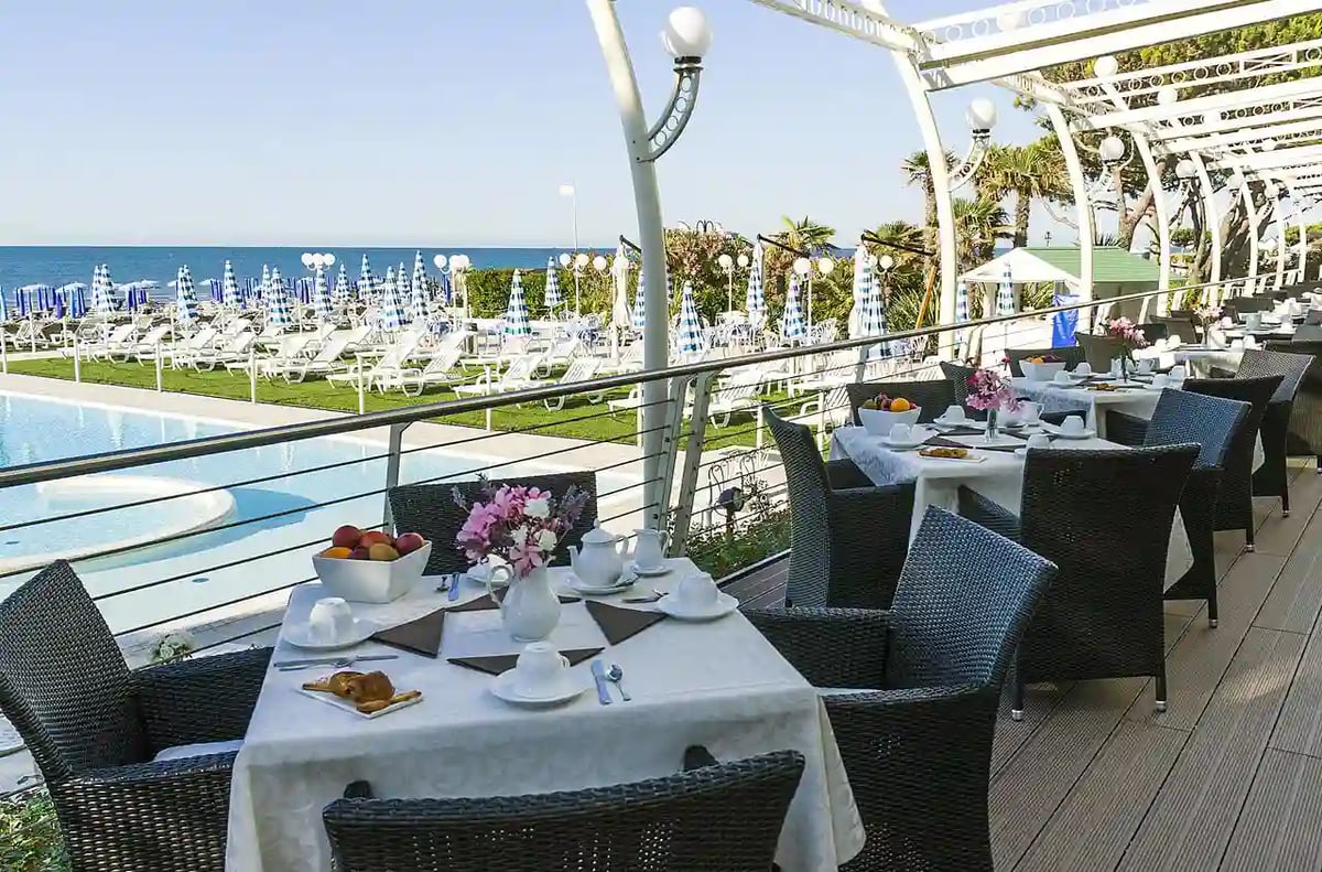 Gedeckte Tische auf einer Terrasse mit Blick auf Pool, Liegen und das Meer