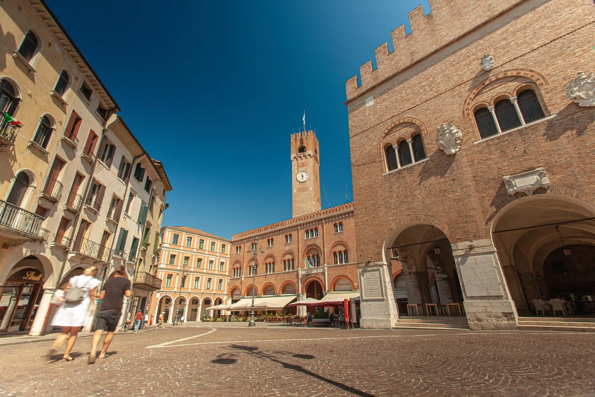 Historischer Platz in Treviso mit Backsteingebäuden, Uhrturm und Menschen beim Spaziergang