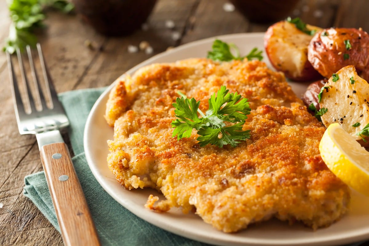Knuspriges Wiener Schnitzel mit Petersilie, Zitronenspalte und Bratkartoffeln auf einem Teller