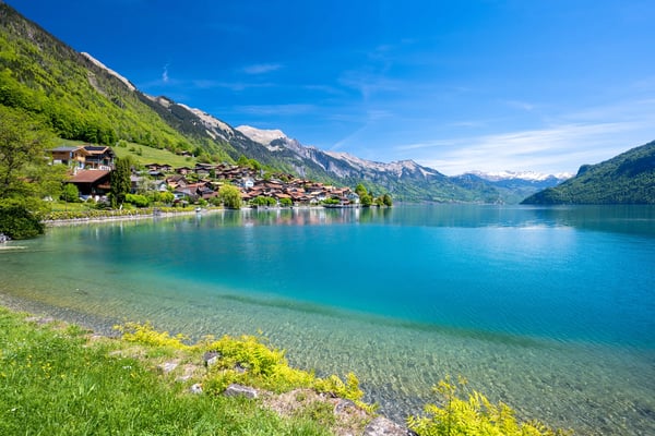 Türkisfarbener Brienzersee mit Dorf am Ufer und Alpen im Hintergrund
