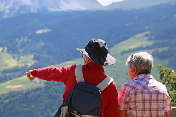 Älteres Paar blickt von einem Aussichtspunkt auf eine weite Berglandschaft