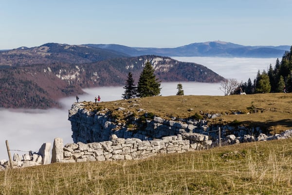 Aussicht von einer Felskante auf eine weite Berglandschaft mit Nebel im Tal und Wanderern im Vordergrund