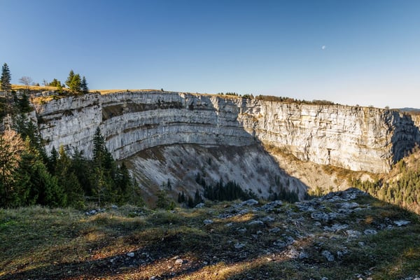 Panoramablick auf die markante Felswand des Creux du Van bei warmem Abendlicht