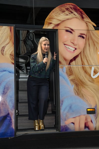 Beatrice Egli steht in der offenen Tür eines Reisebusses und spricht mit einem Mikrofon zu Gästen