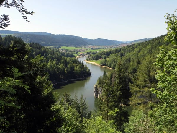 Blick von erhöhter Position auf das Doubs Tal mit Fluss, dichten Wäldern und verstreuten Ortschaften
