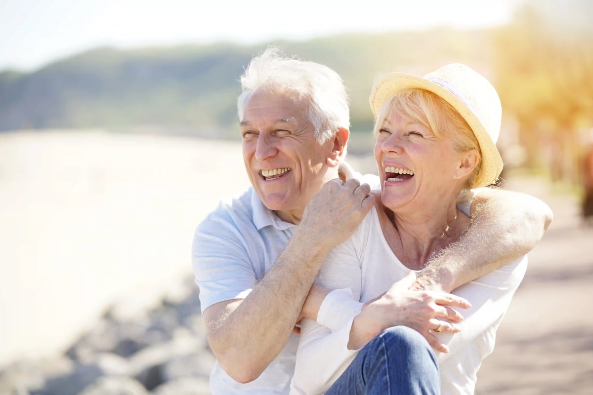 Couple âgé souriant et détendu en plein air, enlacé devant un paysage naturel lumineux