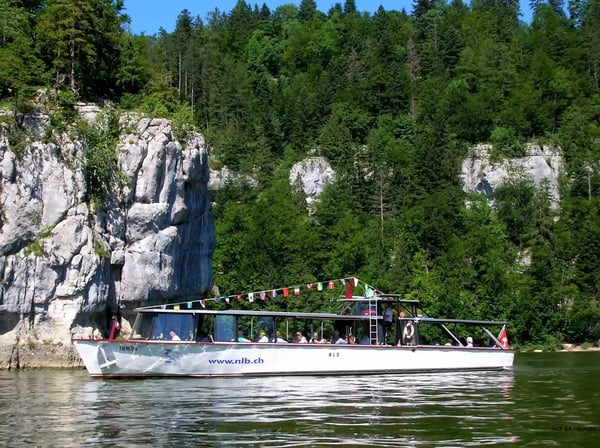 Ausflugsschiff auf der Doubs fährt durch eine enge Flussschlucht mit Felsen und bewaldeten Hängen