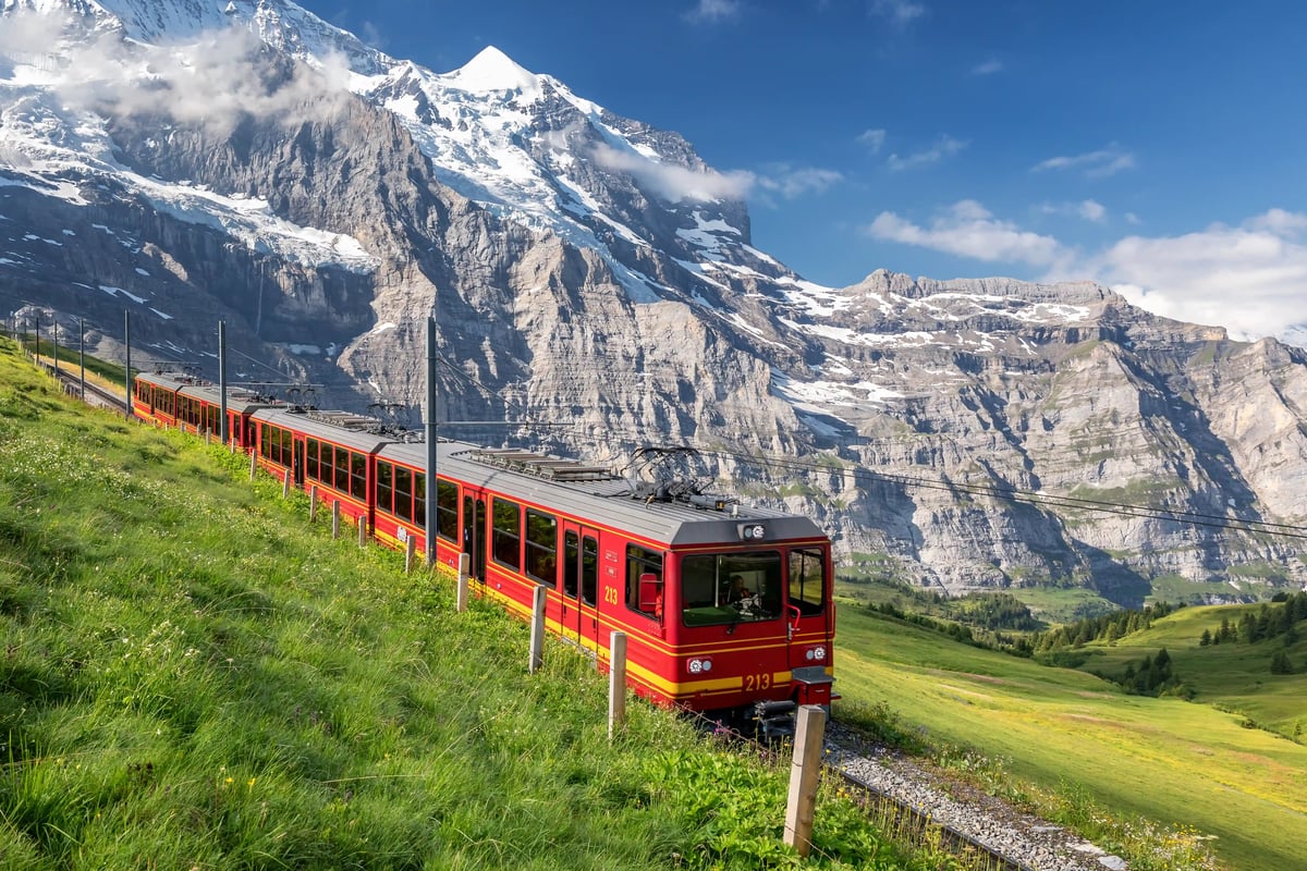 Train rouge de la Wengernalpbahn circulant à travers des prairies alpines devant un décor de glaciers et de sommets escarpés.
