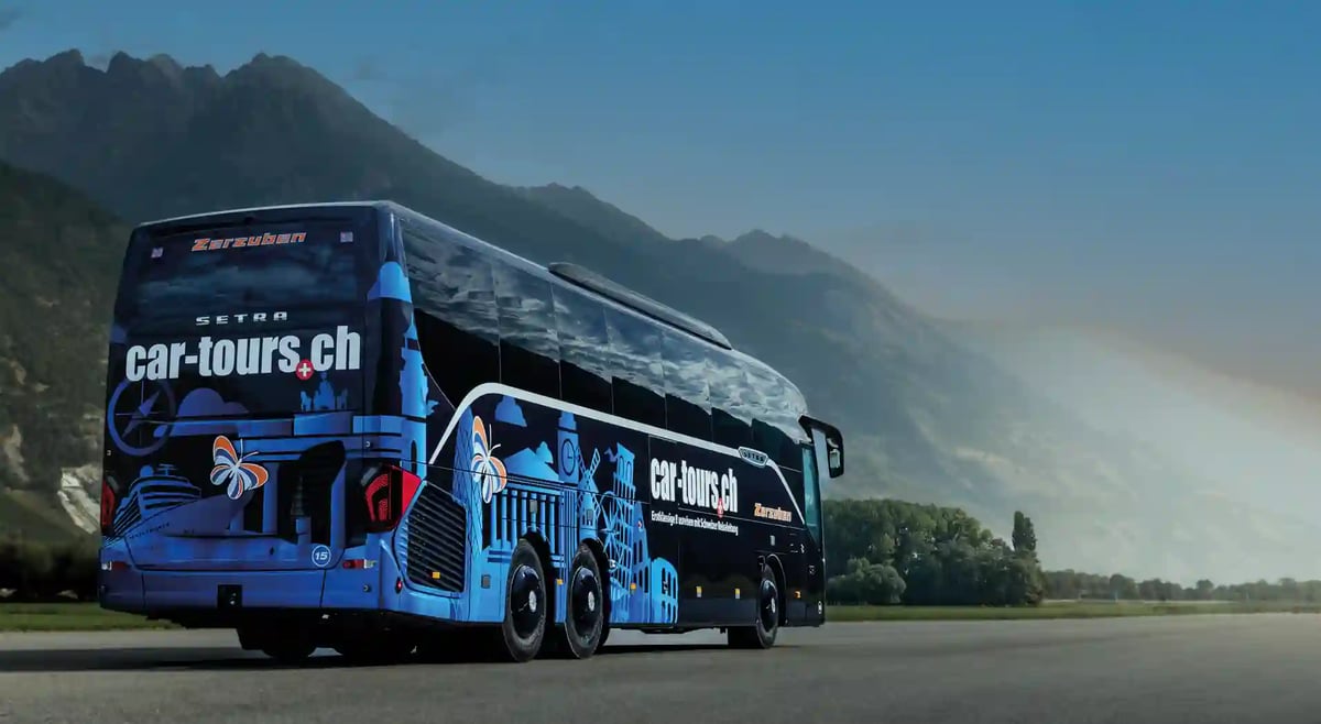 Autocar moderne circulant sur une large route dans une vallée alpine ensoleillée avec des montagnes en arrière plan