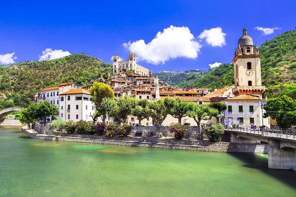 Village pittoresque de Dolceacqua avec pont en pierre, église et maisons historiques au bord de la rivière, entouré de collines verdoyantes sous un ciel bleu